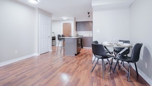 A modern kitchen with a central island, a dining area with a round table and black chairs, and a hallway leading to a door.