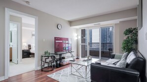 A modern living room with a black leather sofa, a glass coffee table, and a TV on the wall.