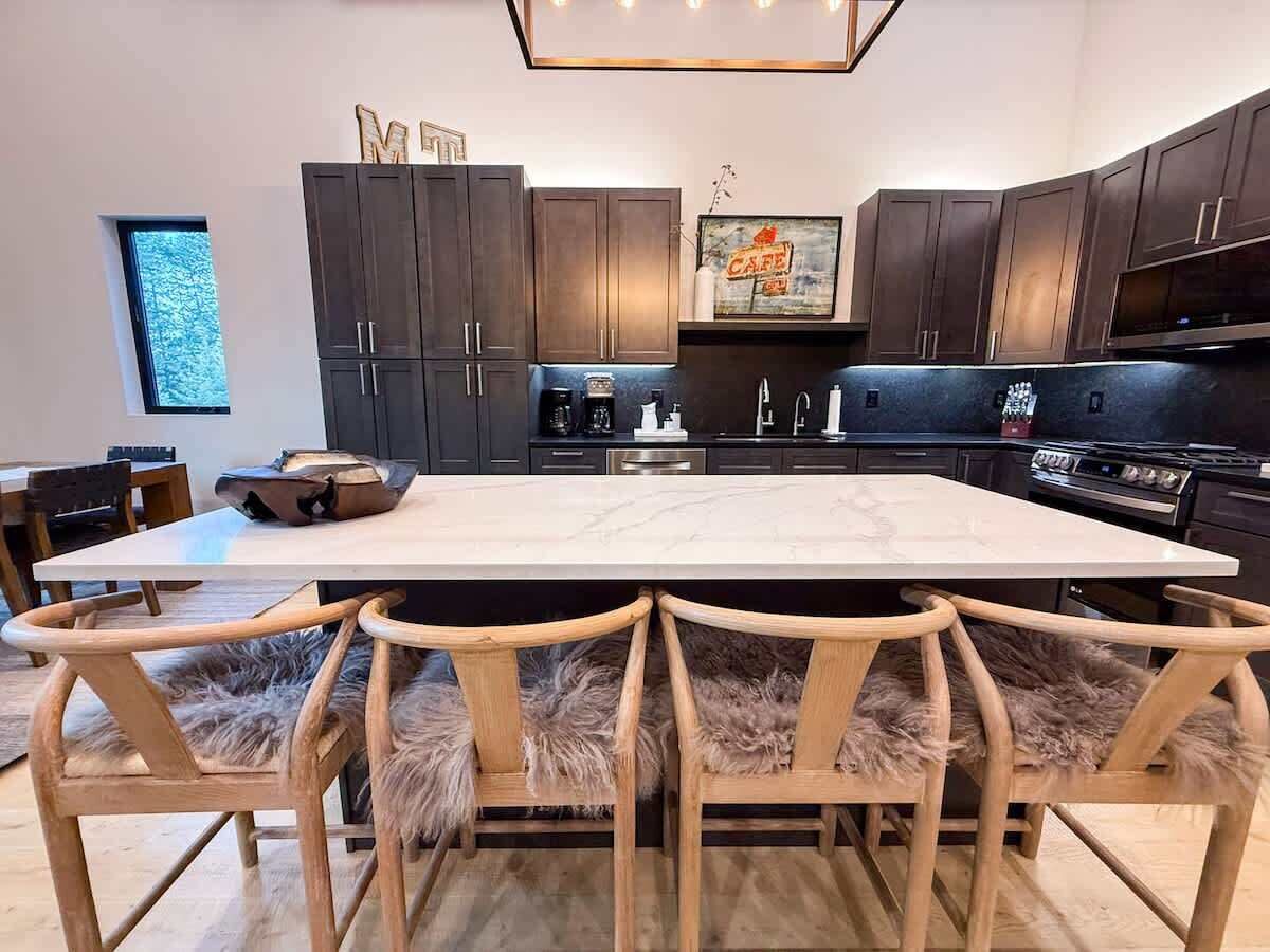 Een moderne keuken met donkere houten kastjes, een marmeren aanrecht en een eethoek met houten stoelen en een zacht tapijt.