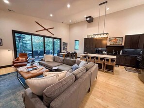 A spacious living room with a large sectional sofa, a dining area with a wooden table, and a kitchen with dark cabinets and a black refrigerator. - Great Location | 4BD/4BA | Hot Tub & Fire Pit (Whitefish)