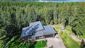Une maison moderne dotée d’un grand garage, entourée d’une forêt dense et avec un lac en arrière-plan.