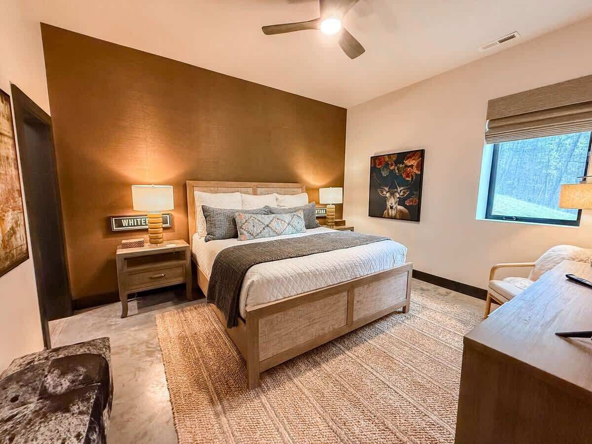 A bedroom with a bed, bedside tables, a desk, a chair, a window, and a ceiling fan.