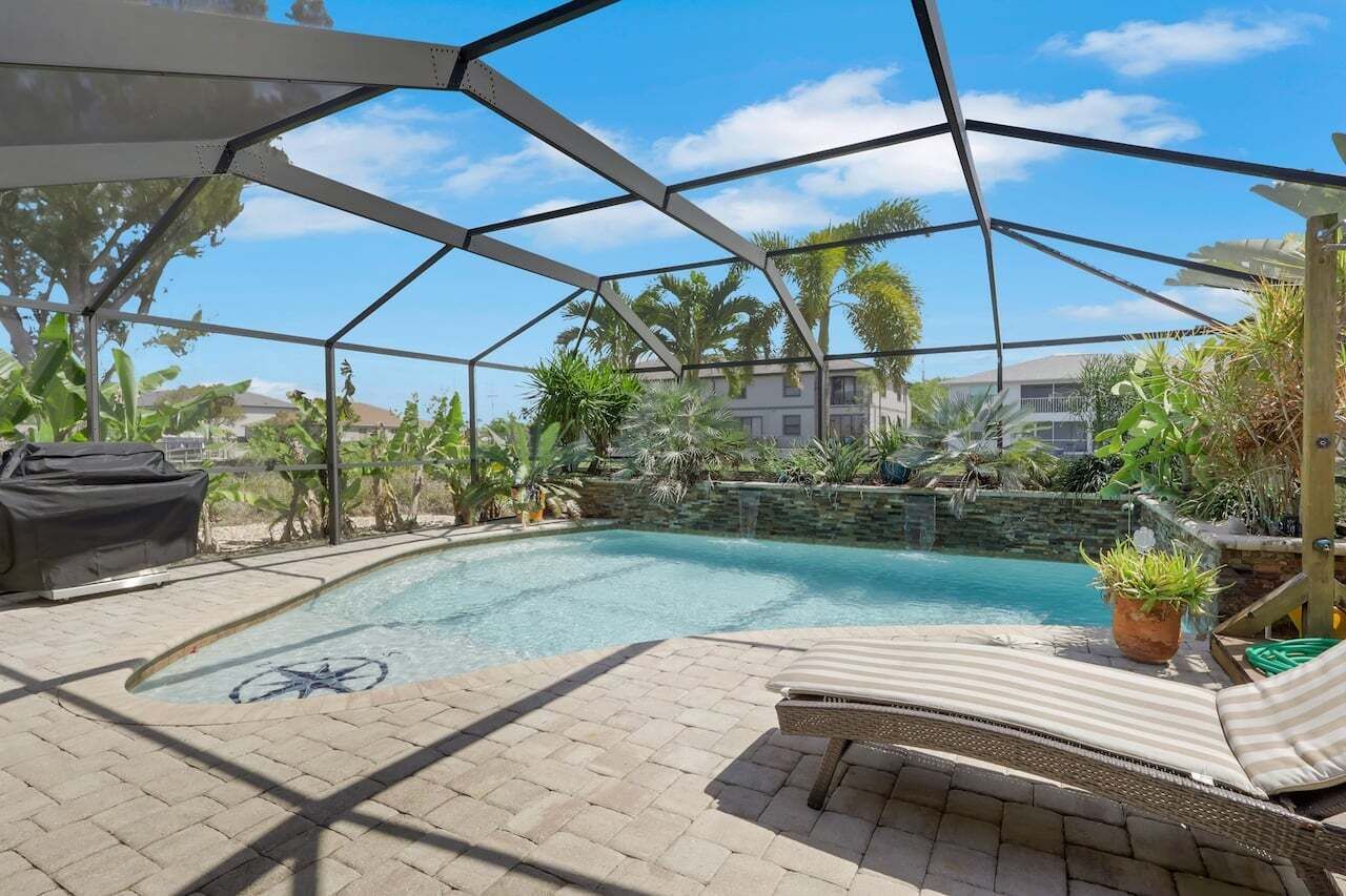 A covered outdoor swimming pool with lounge chairs, potted plants, and a clear view of the surrounding landscape.