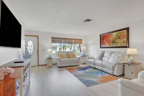 A living room with two sofas, a coffee table, a TV, and a large painting. - Sea Star Dream House 1034 (Cape Coral)