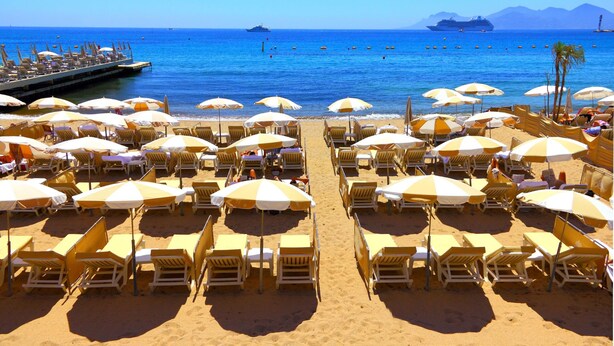 A beach with rows of sun loungers and umbrellas, a pier extending into the water, and a cruise ship in the distance. - Cannes Sea View - Port du Moure Rouge, Cannes, France (Cannes)