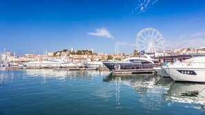 A marina with several yachts docked, a Ferris wheel in the background, and a coastal cityscape. - Cannes Sea View - Port du Moure Rouge, Cannes, France (Cannes)