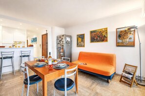 A modern living room with a wooden dining table, two chairs, a sofa, and a coffee table. There are framed artworks on the walls and a lamp on a side table. - Cannes Sea View - Port du Moure Rouge, Cannes, France (Cannes)
