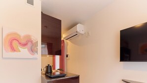 Una camera d'albergo moderna con televisione a schermo piatto, condizionatore d'aria, un quadro appeso al muro e un piccolo angolo cottura.