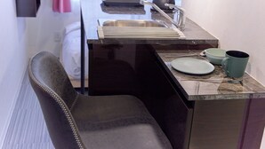 Una cucina compatta con lavandino, bollitore e una sedia.