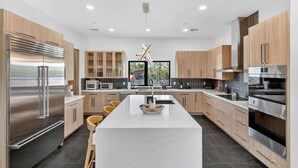 Een moderne keuken met een centraal eiland, roestvrijstalen apparatuur, houten kasten en een groot raam.