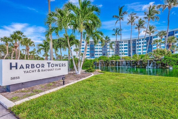 Naamplaatje voor Harbor Towers Yacht & Racquet Club, met uitzicht op een waterpartij en palmbomen.