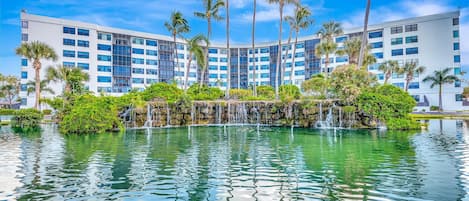 A modern hotel with a central water feature, palm trees, and a clear blue sky.