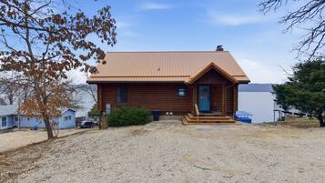 A wooden cabin with a metal roof, a front porch, and a gravel driveway.