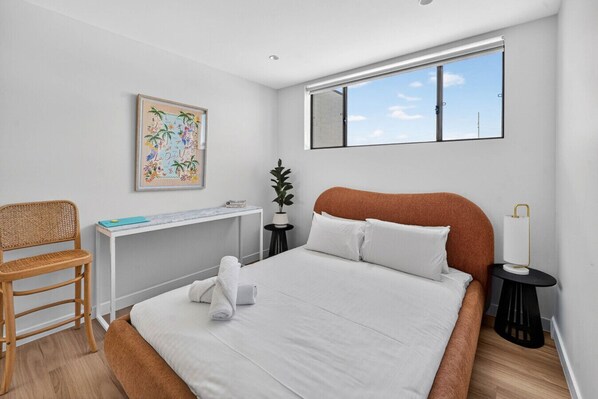 A modern bedroom with a large bed, a desk, a chair, a potted plant, and a window with a view of the sky. - Bonanza Lane Hideaway (Sans Souci)