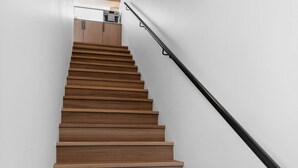 Una scala in legno con ringhiera nera che conduce a una stanza con una porta di legno e una parete bianca.