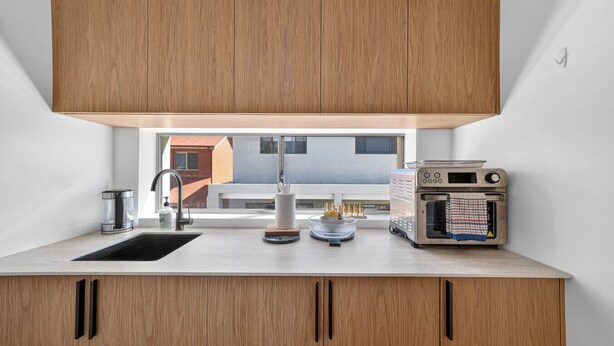 Una cucina moderna con mobili in legno, un lavello in acciaio inossidabile, forno integrato e una finestra vista su zona residenziale.