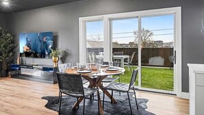 En moderne stue med spiseplads, store skydedøre til en baghave og et fladskærms-tv på væggen.