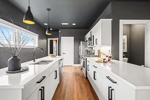 A modern kitchen with white cabinetry, a central island, pendant lighting, and a view of the outdoors. - Sunset-Expansive Patio & Hot Tub-Mins to Broadway (Nashville)