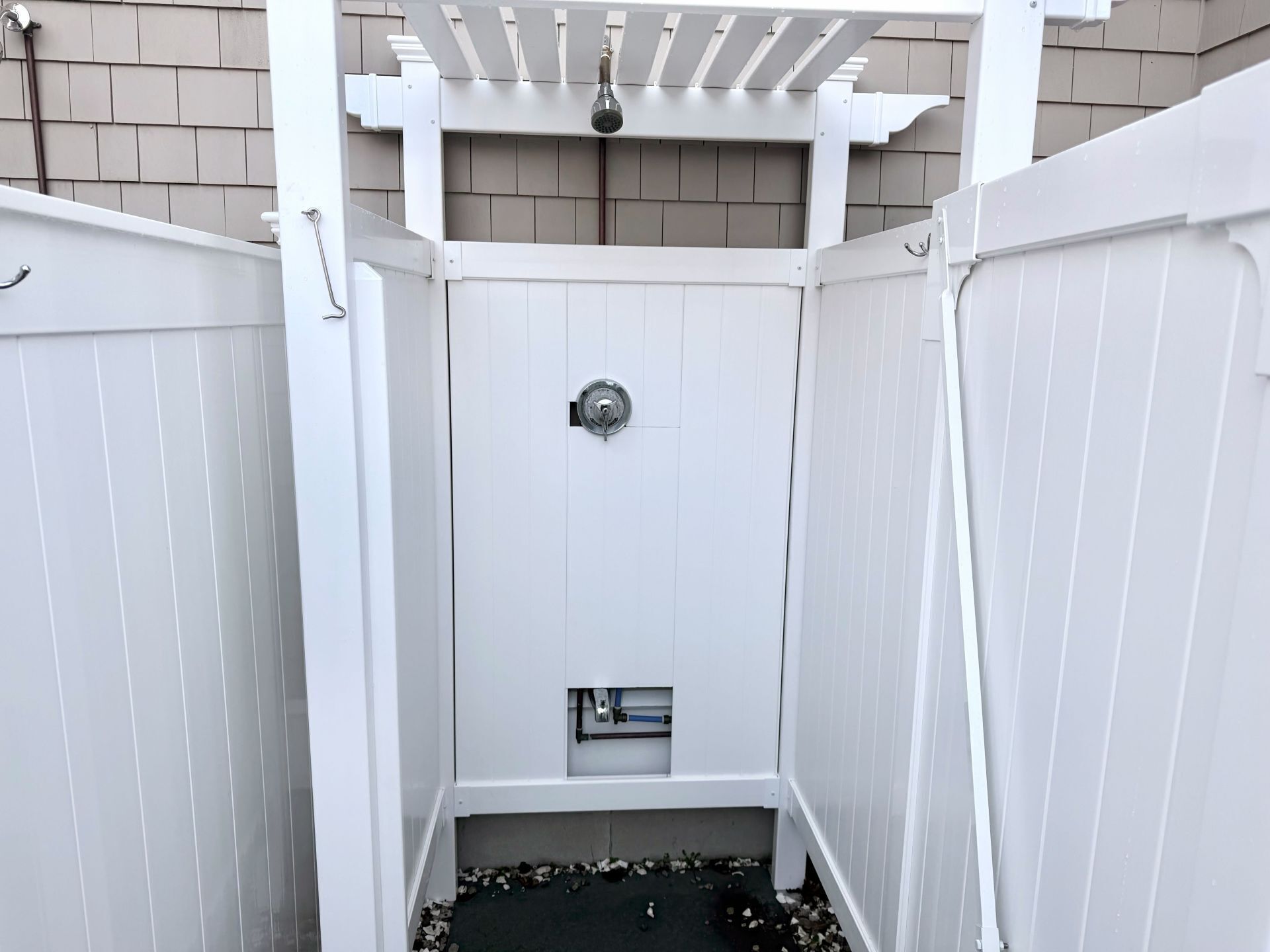 A white outdoor shower enclosure with a showerhead and a small shelf.