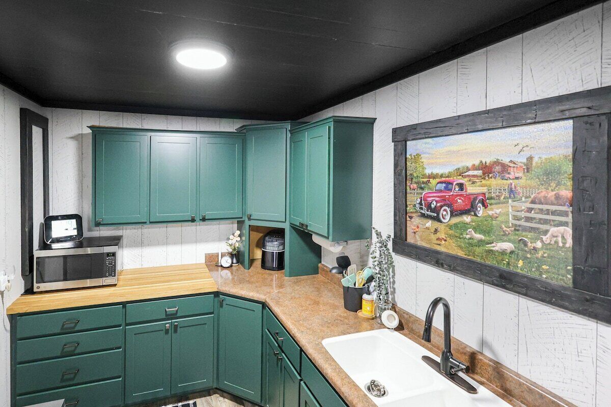 A kitchen with green cabinets, a microwave, a sink, and a painting of a red truck on the wall.