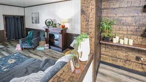 Una habitación con piso de madera, un sofá, una silla, una chimenea y un estante con velas.