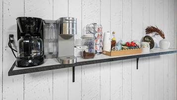 A kitchen counter with a coffee maker, a kettle, a jar of sugar, a honey dispenser, a box of tea bags, and a decorative vase.