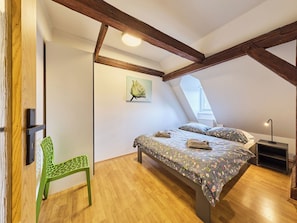 Ein Schlafzimmer mit Schräge, einem Bett mit floralem Bettbezug, einem grünen Sessel und einem Nachttisch mit Lampe.