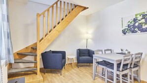 A staircase leading to an upper floor, a dining area with a table and chairs, and a single blue armchair. - Růžová 4 by Interhome (Ruzova)
