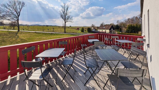 An outdoor deck with tables and chairs, overlooking a grassy field and a village. - Růžová 4 by Interhome (Ruzova)