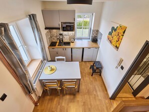 A compact kitchen with a dining area, a small refrigerator, a microwave, and a window.