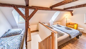 Camera mansarda con travi a vista in legno, un letto con biancheria da letto floreale, una poltrona gialla e un tavolino.