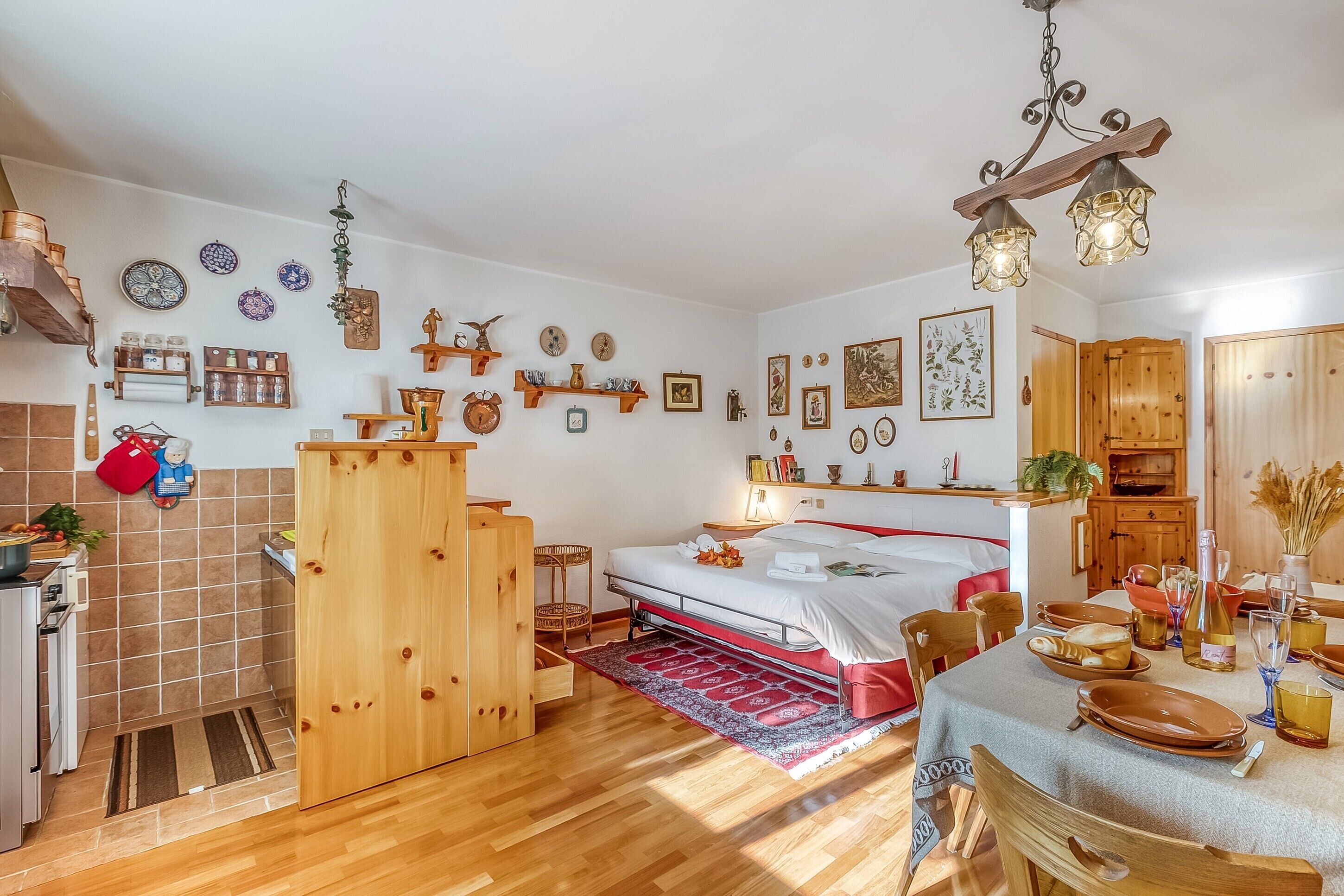 A cozy, well-lit room with a bed, wooden furniture, a dining table set, and various wall decorations.