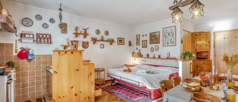 A cozy, well-lit room with a bed, wooden furniture, a dining table set, and various wall decorations.
