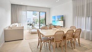 A modern living room with a dining area, a sofa, and a TV. - Luxe on Sandringham San Souci Sanctuary (Sans Souci)