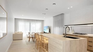 A modern kitchen with a central island, dining area with chairs, and a large window with curtains. - Luxe on Sandringham San Souci Sanctuary (Sans Souci)