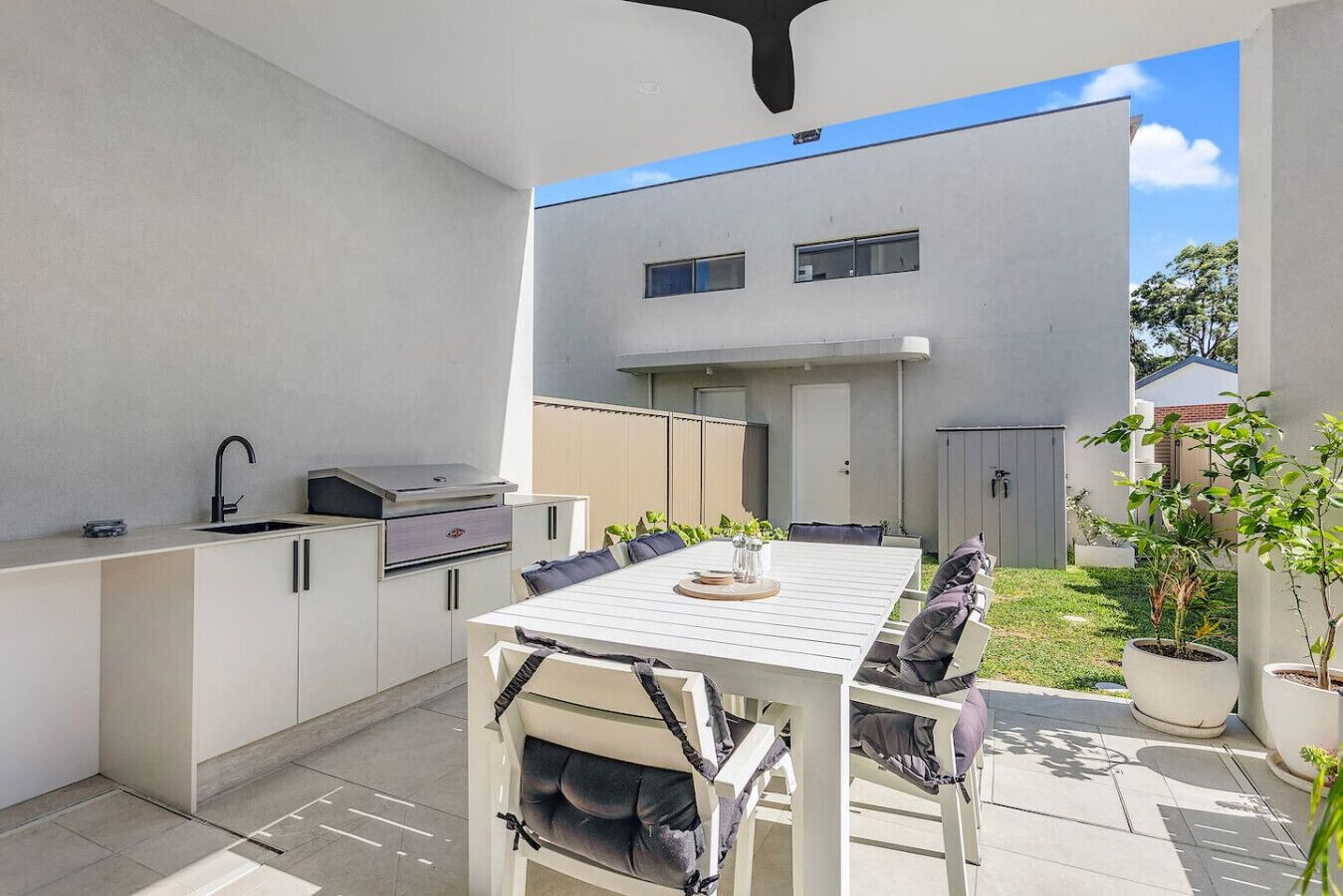 Een moderne buitenkeuken met een eettafel, stoelen, een barbecue en een ingebouwde spoelbak.