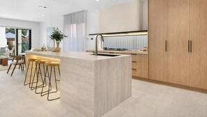 A modern kitchen with a central island, bar stools, and wooden cabinets. - Luxe on Sandringham San Souci Sanctuary (Sans Souci)