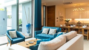 A modern living room with a sofa set, a coffee table, and a dining area with a table and chairs. - Luxury Teak 4BR Private Pool Villa in Bang Tao (Choeng Thale)