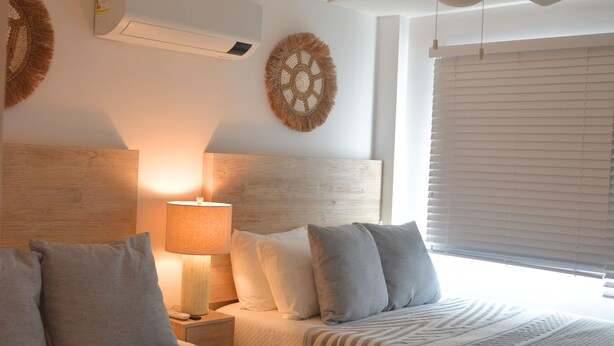 Ein Schlafzimmer mit zwei Betten, einem Deckenventilator, einer Wandklimaanlage und einem Fenster mit Jalousien.