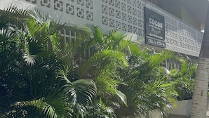 Eine Gebäudefassade mit geometrischem Muster, ein Schild mit der Aufschrift 'Cocos Apartments' und üppigem Grün.