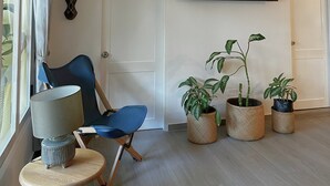 Ein modernes Wohnzimmer mit blauem Sessel, einem kleinen runden Tisch mit Lampe und drei Blumentöpfen.