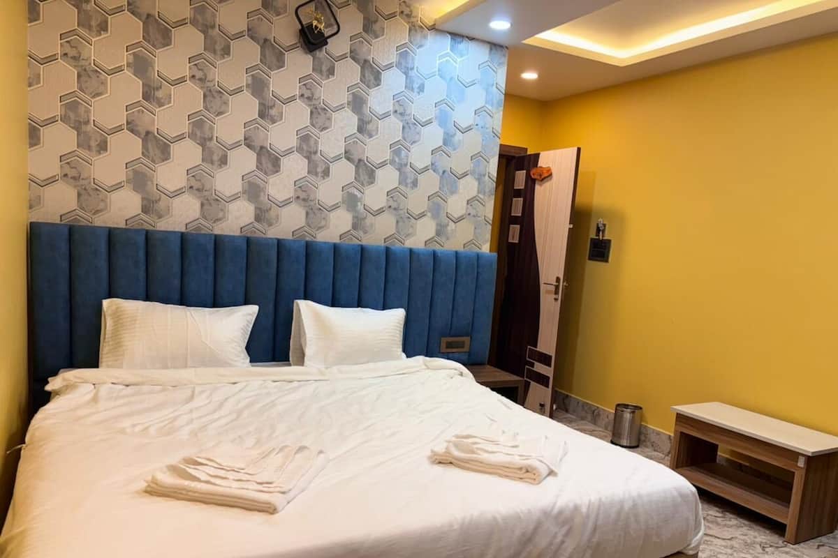A neatly made bed with white linens and towels, a blue upholstered headboard, and a patterned wall behind it.