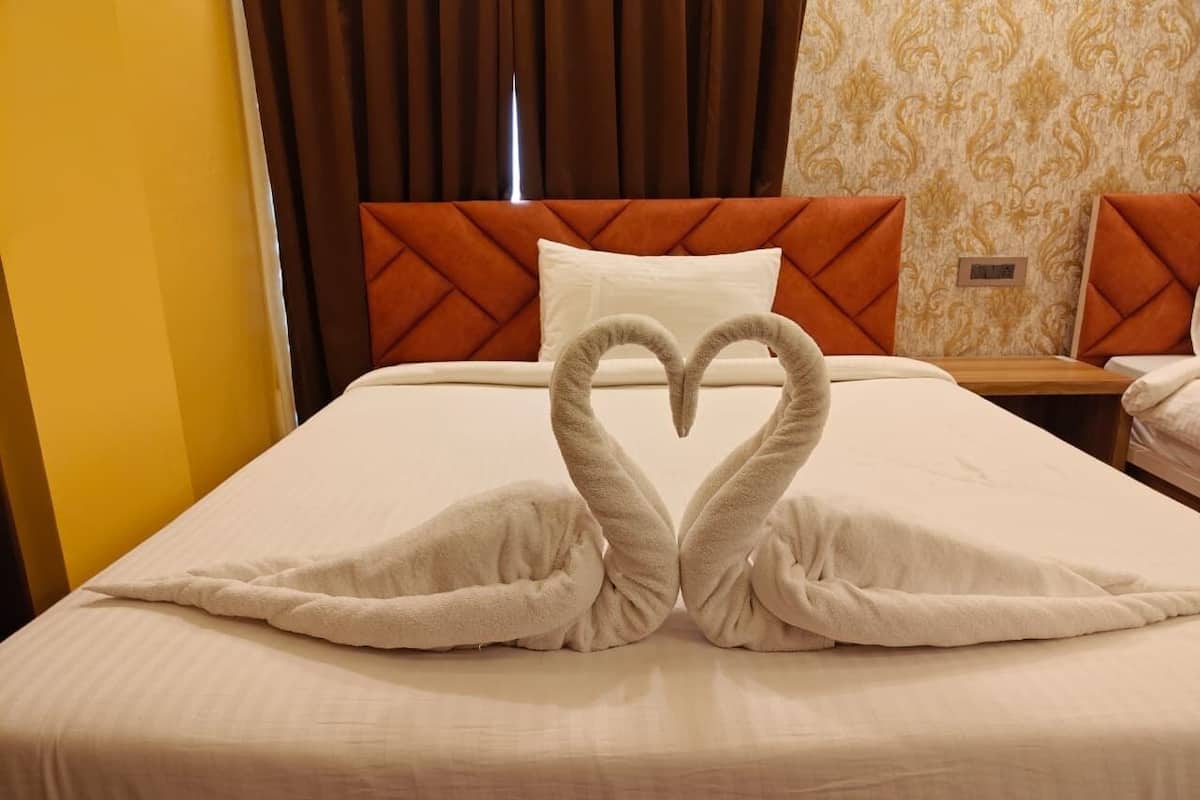A hotel room with a bed, a heart-shaped towel arrangement, a nightstand, and a wall clock.