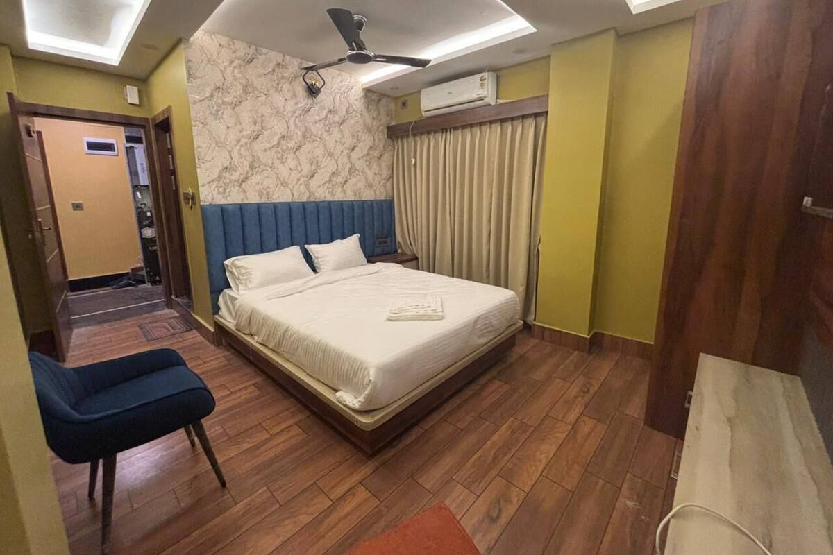A hotel room with a bed, a chair, a ceiling fan, and an air conditioning unit.