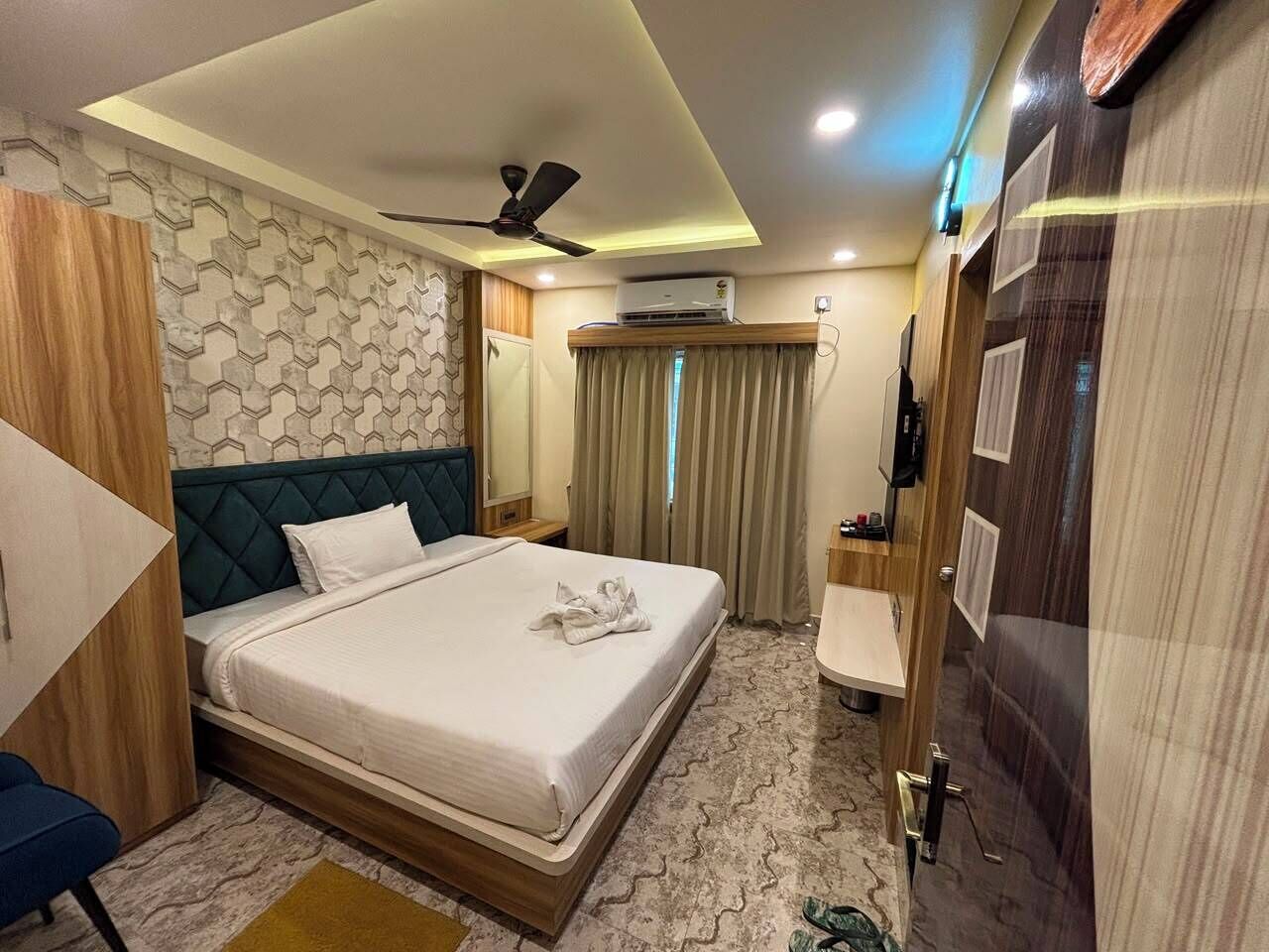 A hotel room with a bed, a desk, a chair, a ceiling fan, an air conditioning unit, and a door.