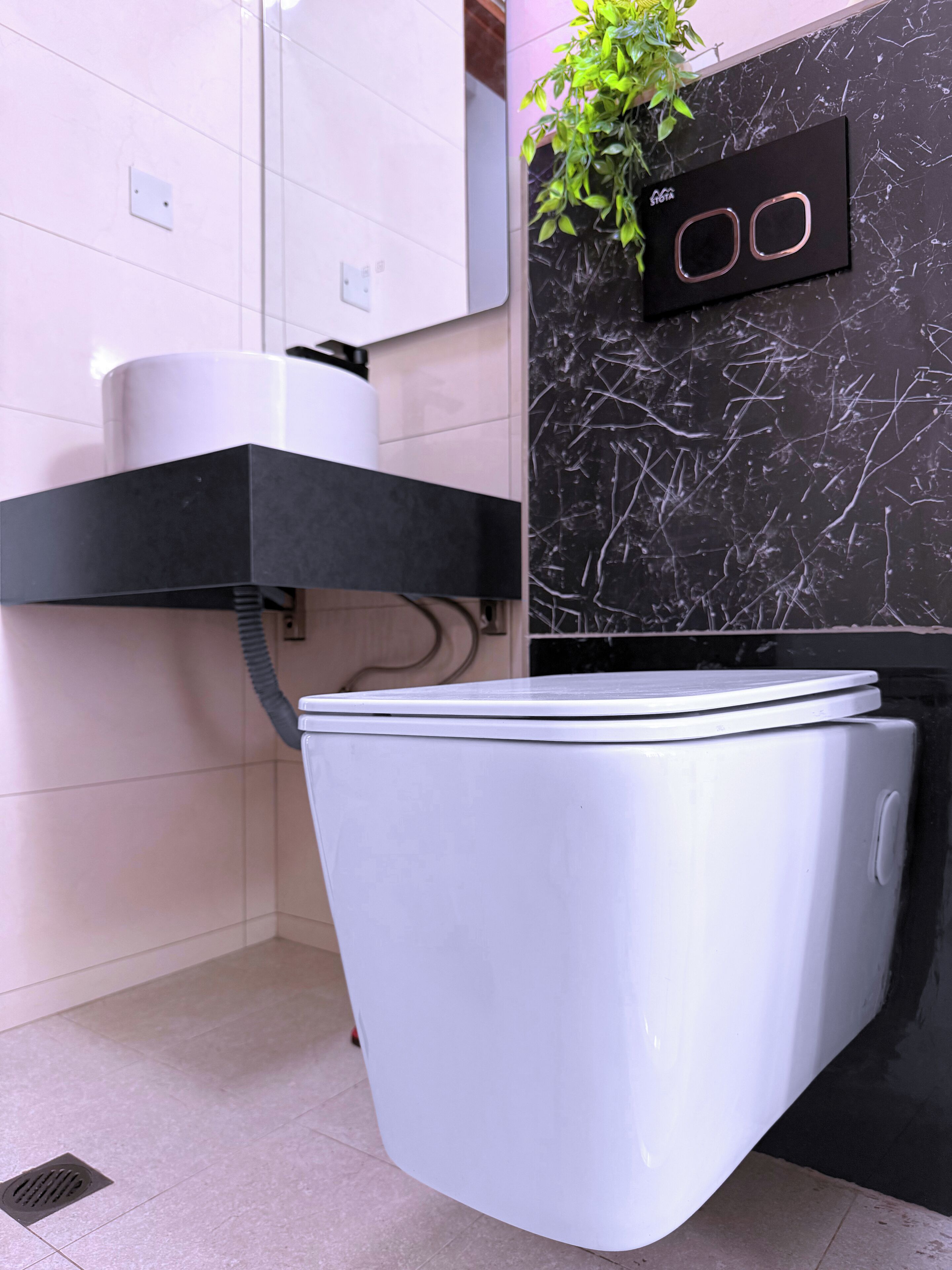 A compact, modern bathroom with a white toilet, a black sink, and a marble backsplash.