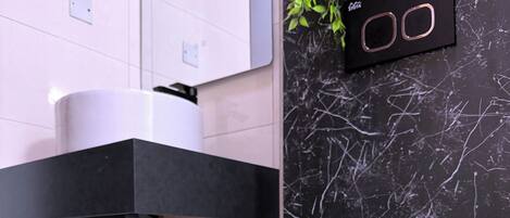 A compact, modern bathroom with a white toilet, a black sink, and a marble backsplash.