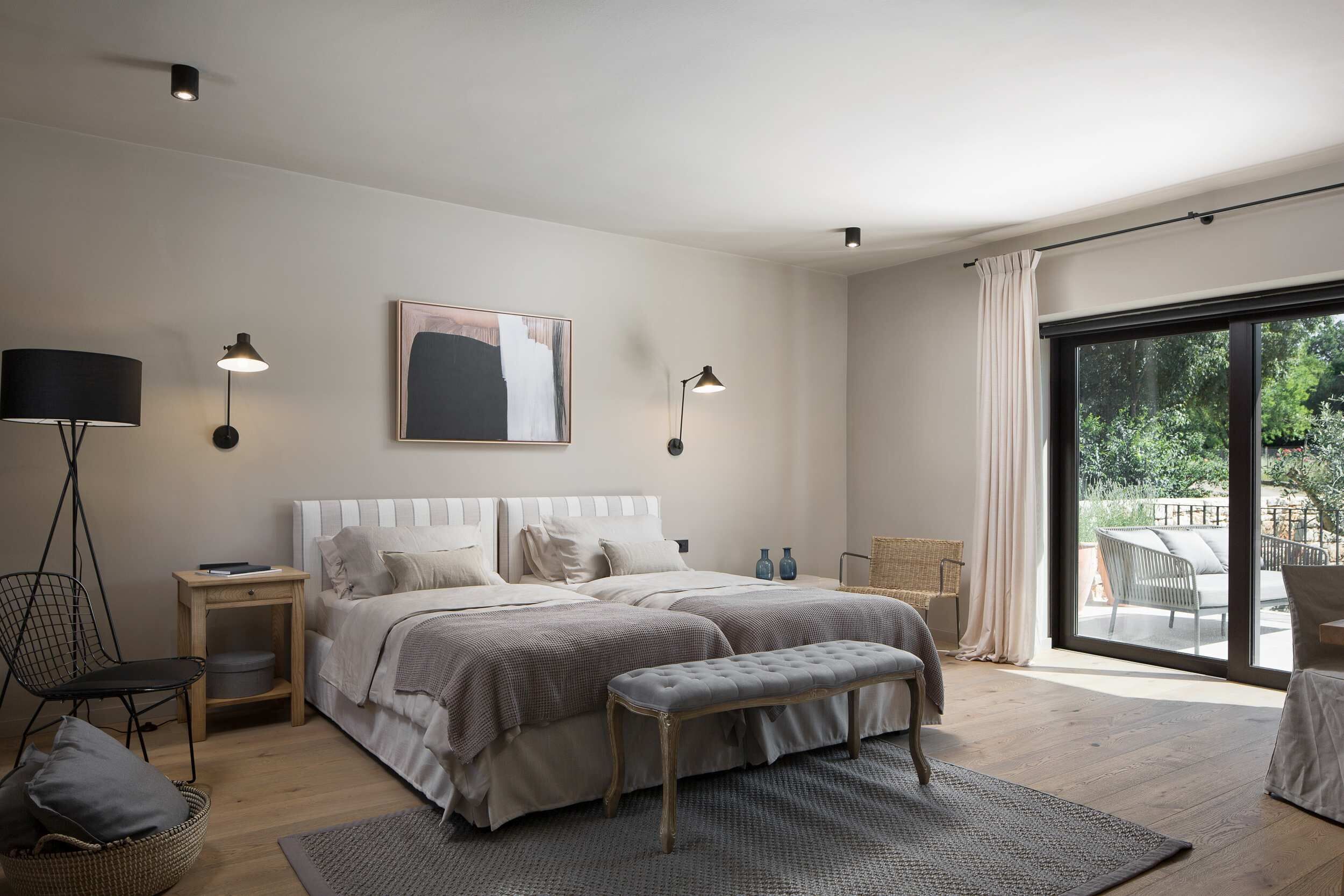 Une chambre moderne avec un grand lit, des tables de chevet, un banc et une vue sur l’extérieur grâce à une porte-fenêtre coulissante.