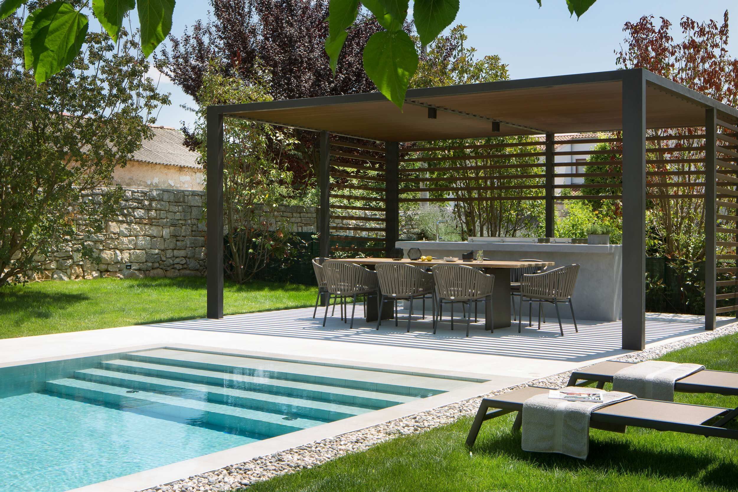 Area piscina con pergola, posti a sedere all'aperto e un muro in pietra sullo sfondo.