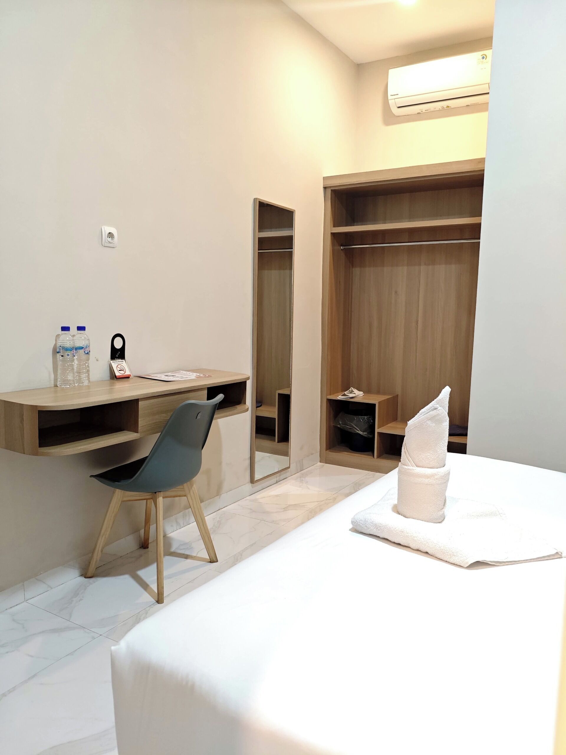 Een hotelkamer met een bed, een bureau met stoel, een kledingkast en een spiegel.